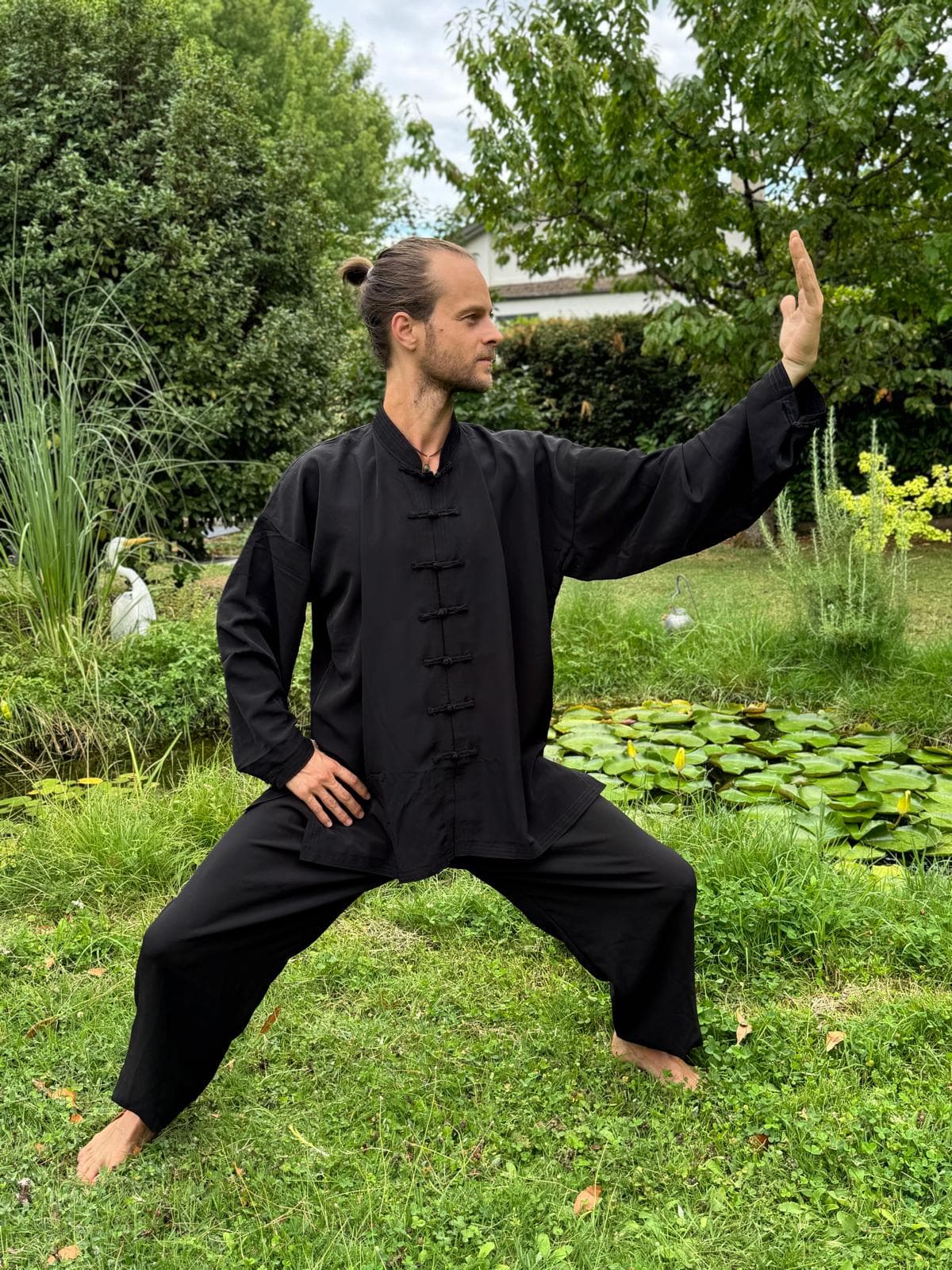 Romain en posture de Qi-Gong, fente large et paume levée, dans le jardin